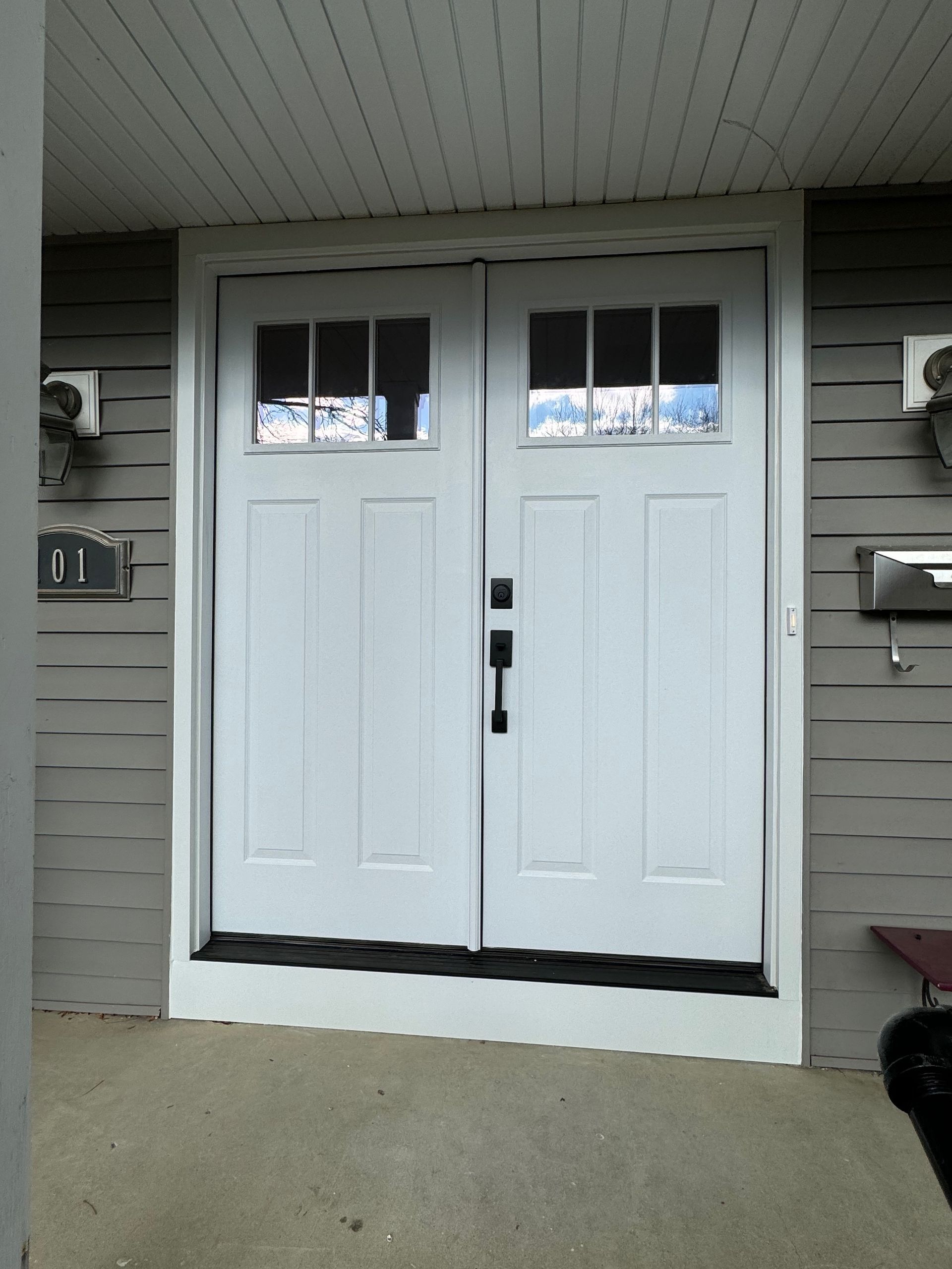 White double doors with glass panels; entry to a building with gray siding.
