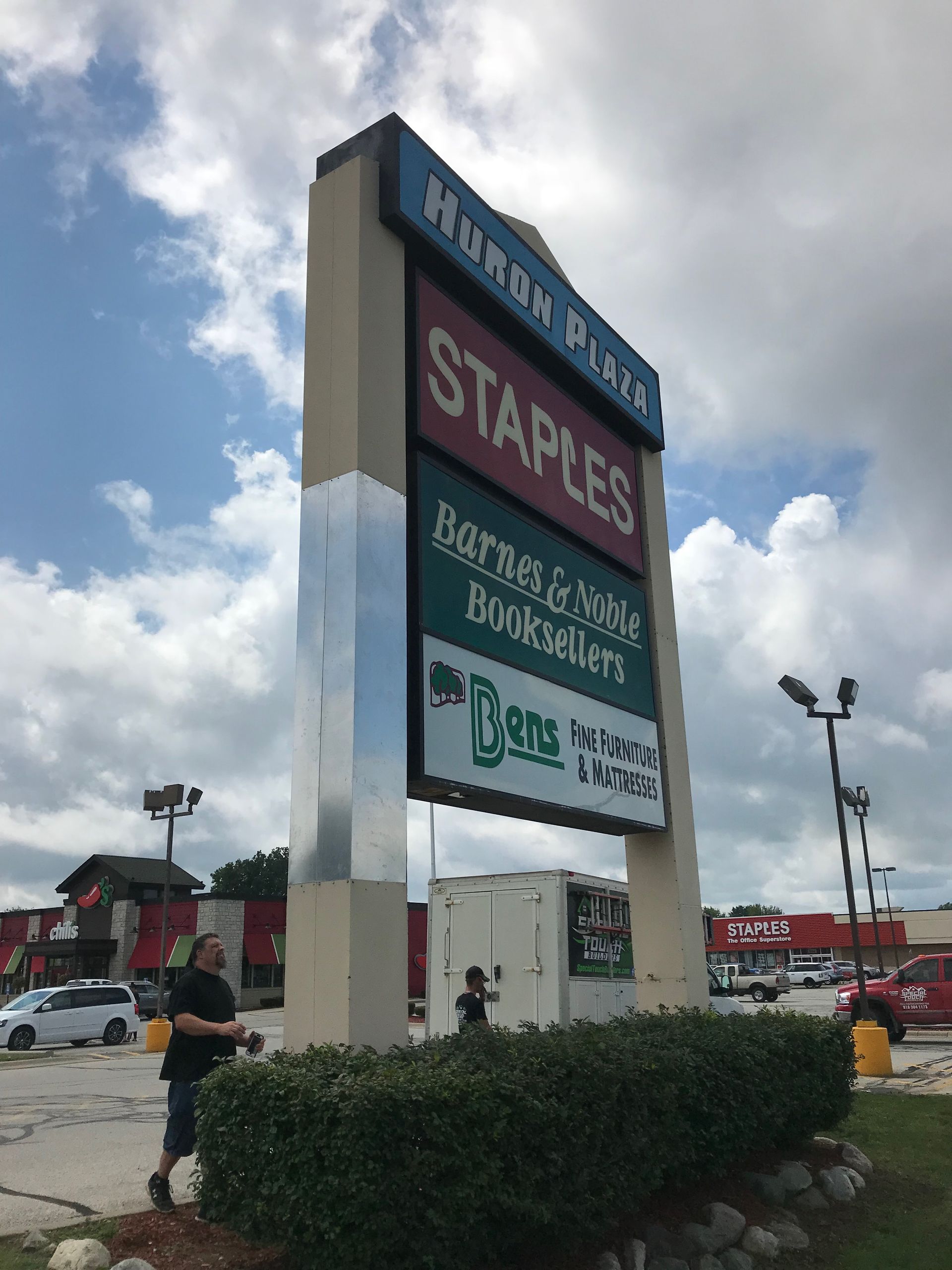 Sign for Harbor Plaza: Staples, Bass Pro Shops, and other businesses. Person tending to shrubs.