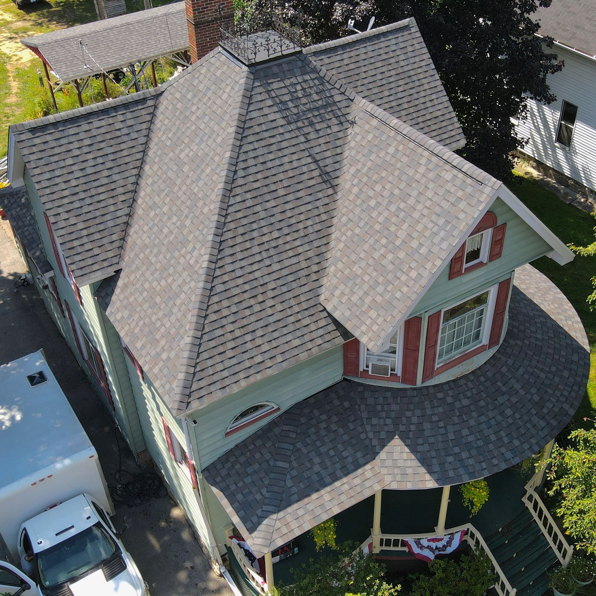 Aerial view of a Victorian-style house with green siding, a gray roof, and a rounded porch with red shutters.
