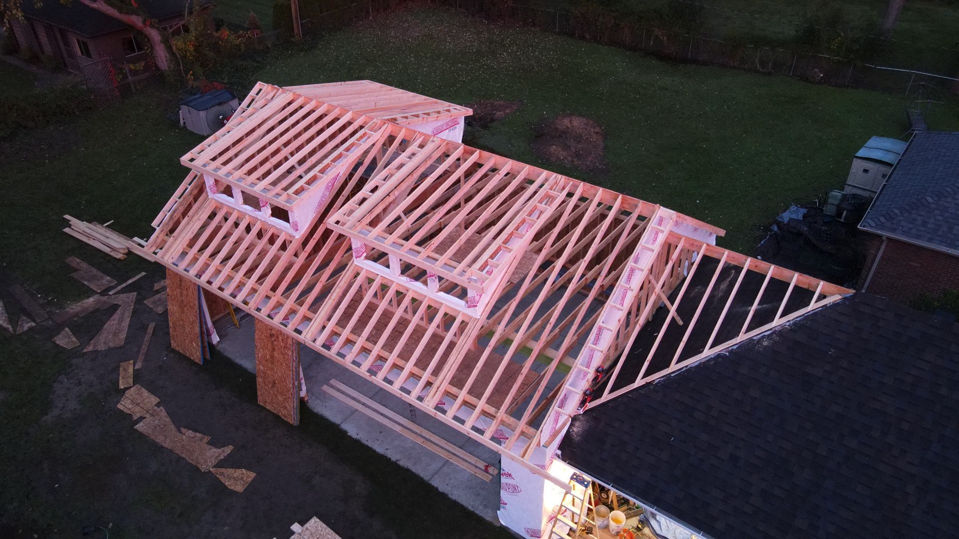 Overhead view of a building under construction, wooden roof framing, dormers, set in a yard.