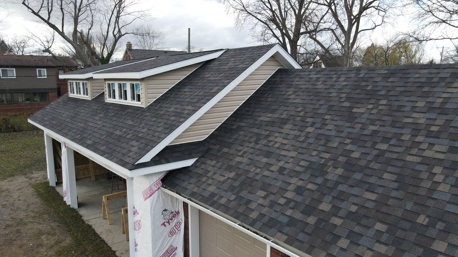 Newly constructed building with gray shingles, beige siding, and white trim. Three windows on the roof.