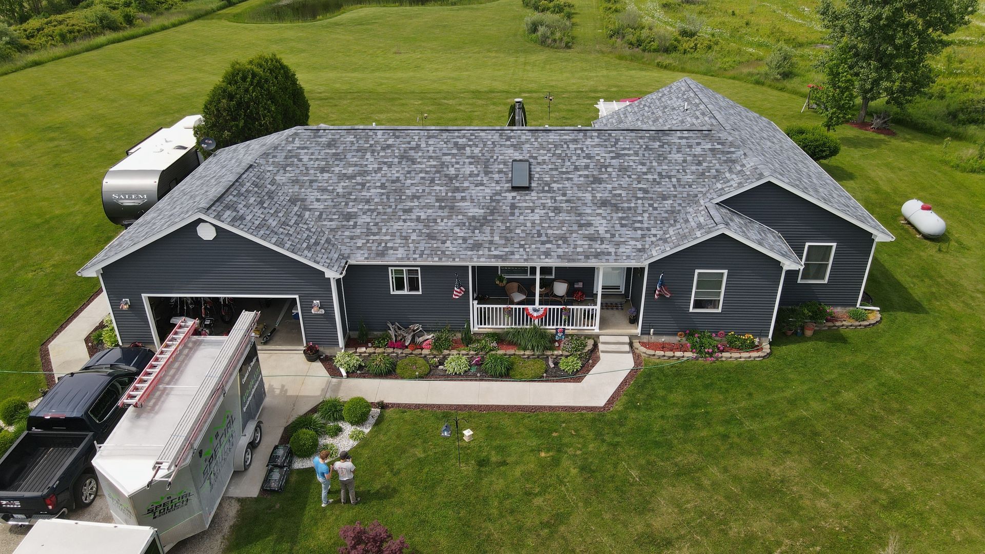 Aerial view of a gray house with a newly installed roof. A white van is parked nearby.
