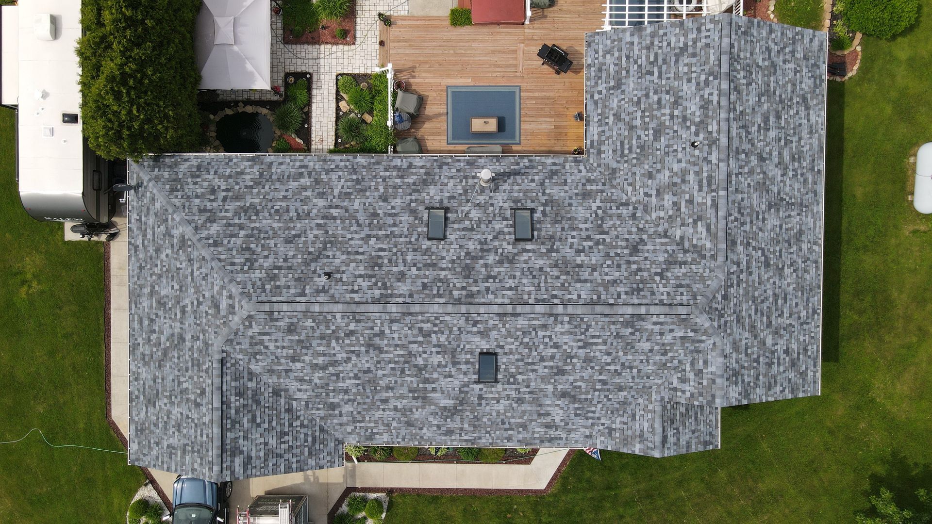Overhead view of a house with a gray shingle roof, three skylights, and a backyard with a deck and pool.