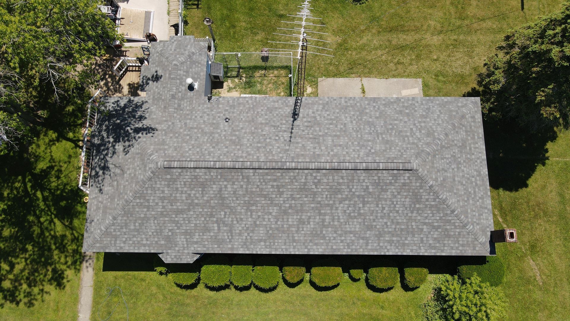 Overhead view of a gray shingle roof on a building with a lawn. Green shrubbery lines the front.