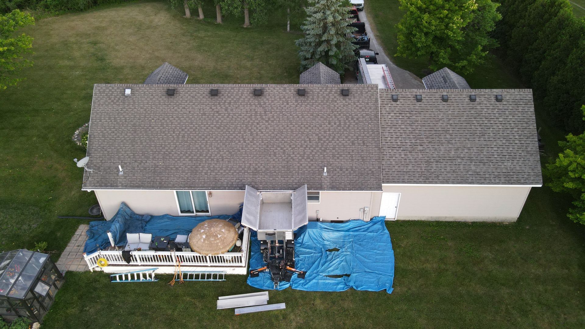 Overhead view of a house with a gray roof, a deck, and a blue tarp covering debris on the ground.