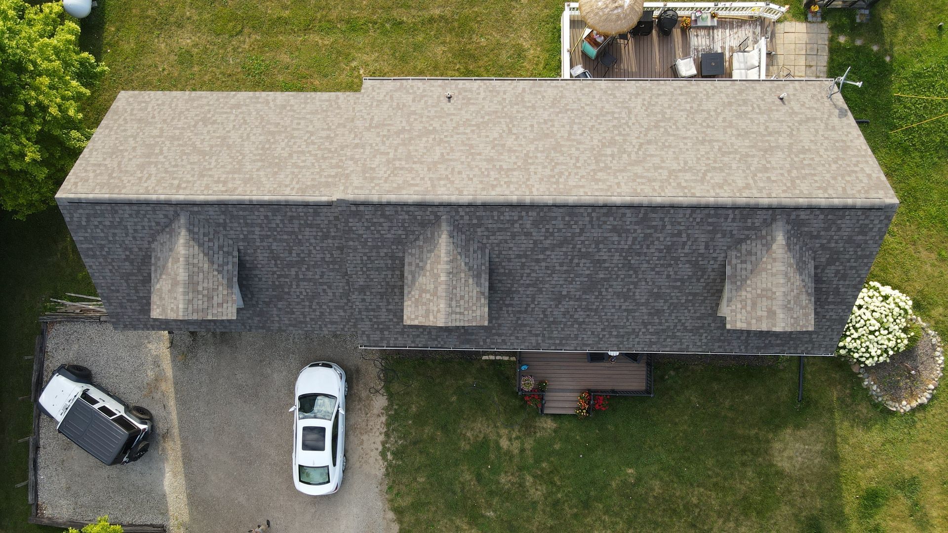 Overhead view of a house with a gray roof, dormers, and two cars parked in the driveway.