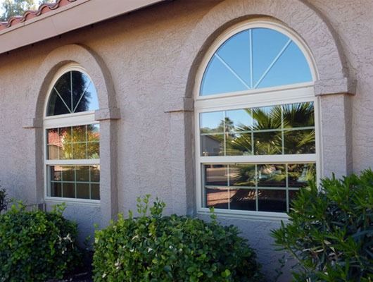 Stucco house facade with two arched windows and green shrubs in front