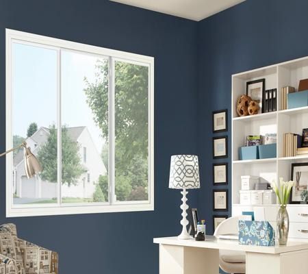 Blue home office with white desk, shelves, and a large window letting in daylight.