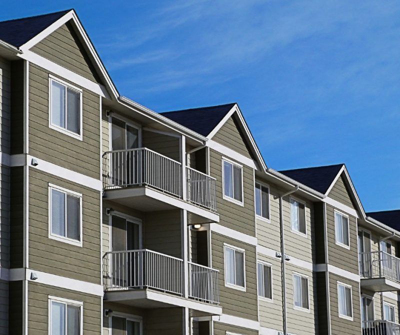 Apartment building with balconies and gray-green siding under a blue sky