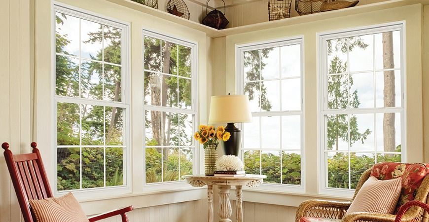 Bright sunroom with large windows, a rocking chair, and a small table with flowers and a lamp.