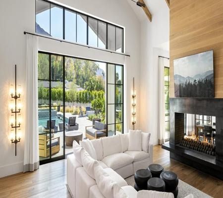 Bright modern living room with white sofa, fireplace, and large glass doors opening to a sunny patio and pool