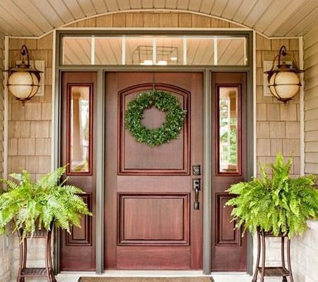 Front porch with a dark wood front door, green wreath, lanterns, and two potted ferns.