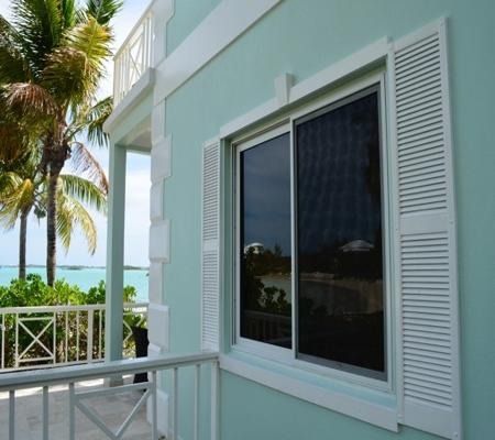 Turquoise house balcony with white shutters, overlooking palm trees and the ocean
