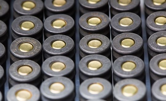 Close-up of rows of dark, cylindrical ammunition with brass-colored primers.