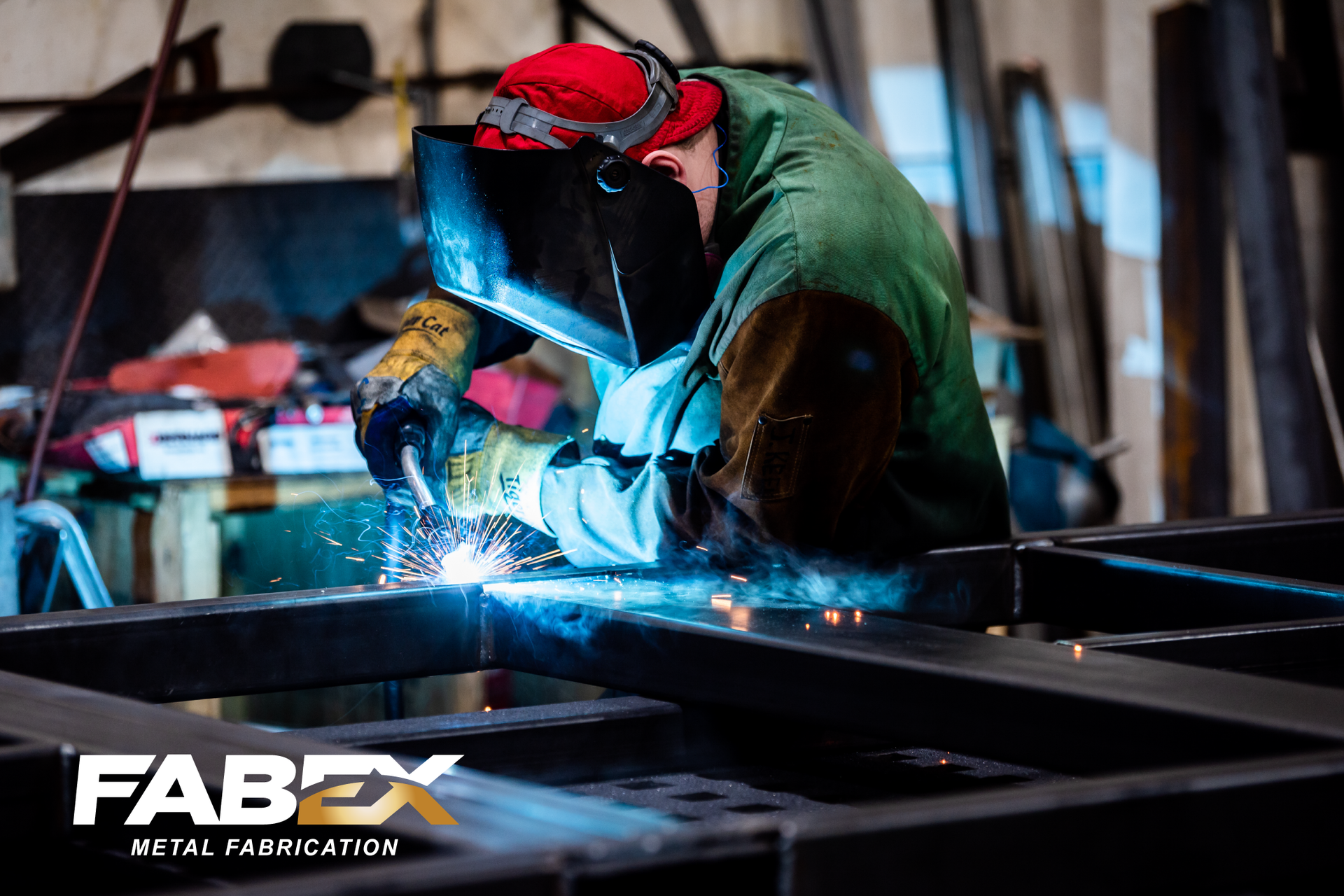 Welder in protective gear welding a metal frame, bright sparks in a workshop with FABEX logo