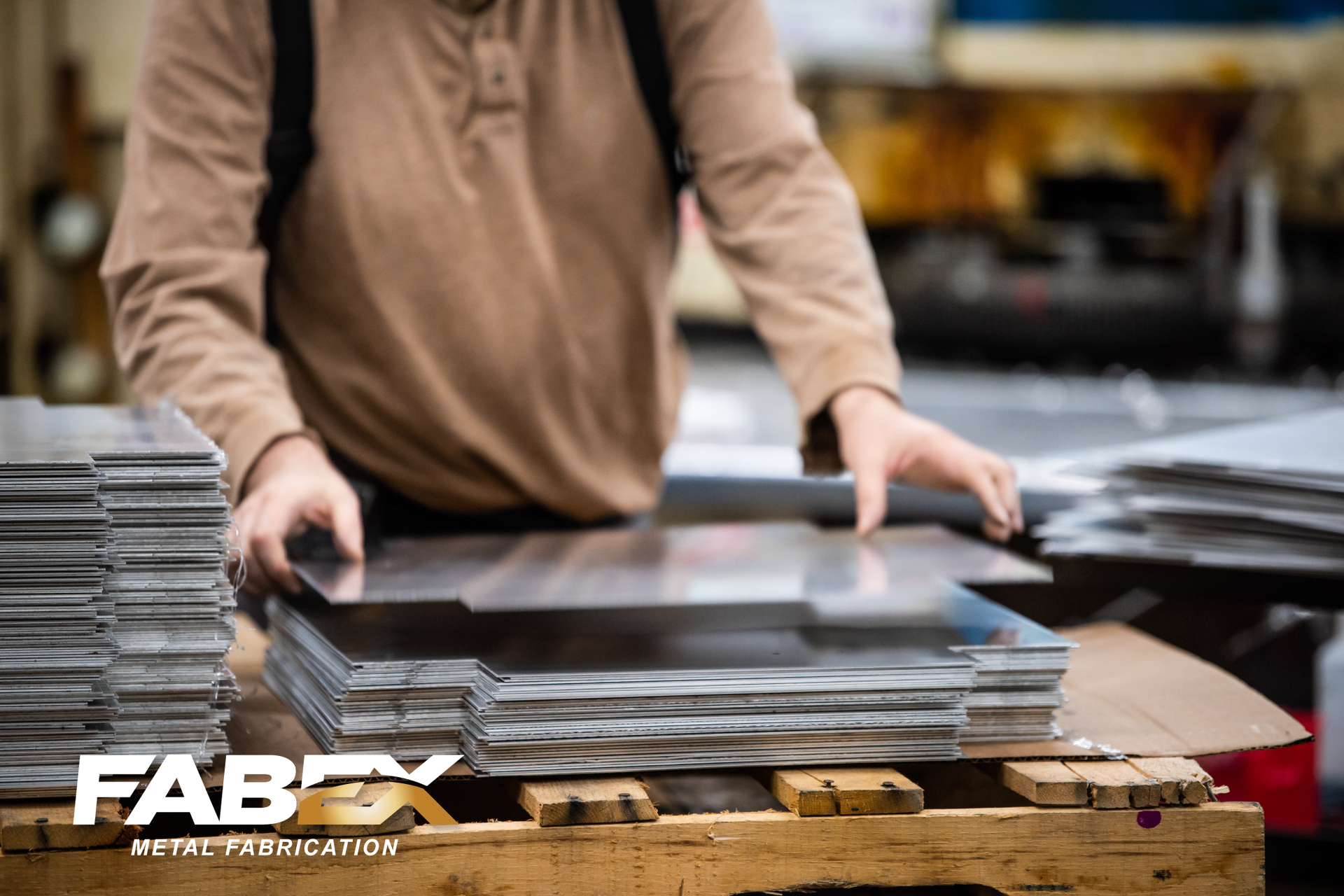 Person stacking flat metal sheets on a workbench in a workshop