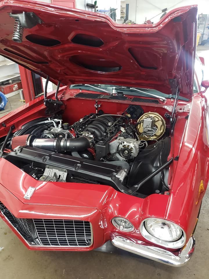 Red classic car with hood open, revealing the engine in a garage.
