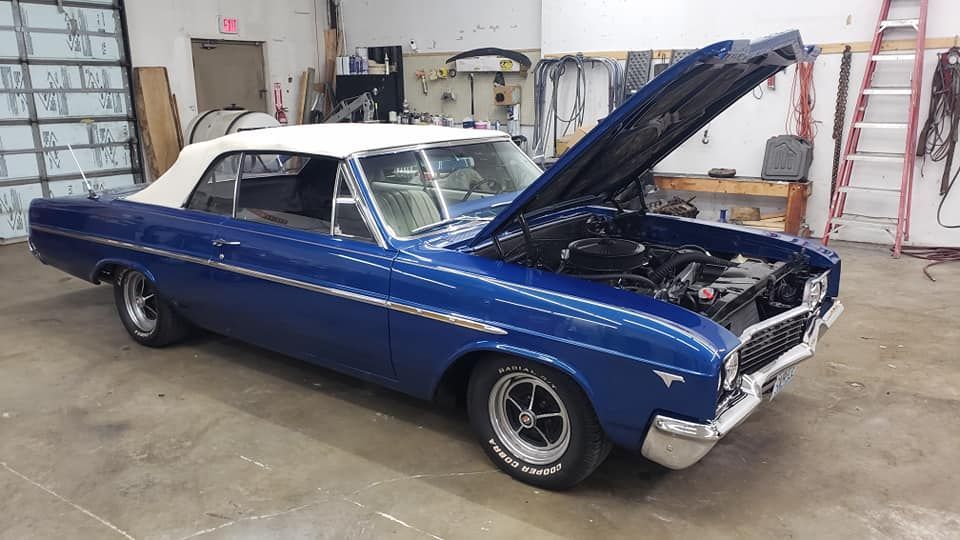 Blue vintage convertible car with white top, hood open, in a garage.