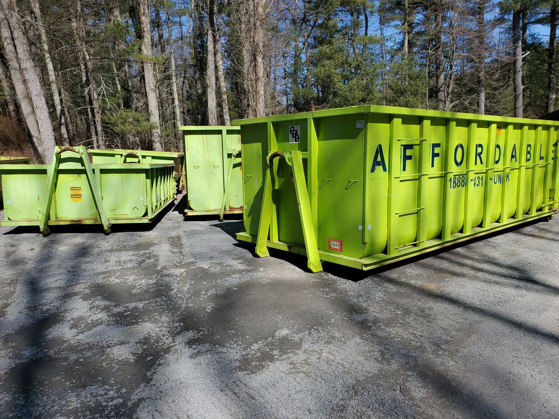 Two green dumpsters are parked next to each other in a parking lot.
