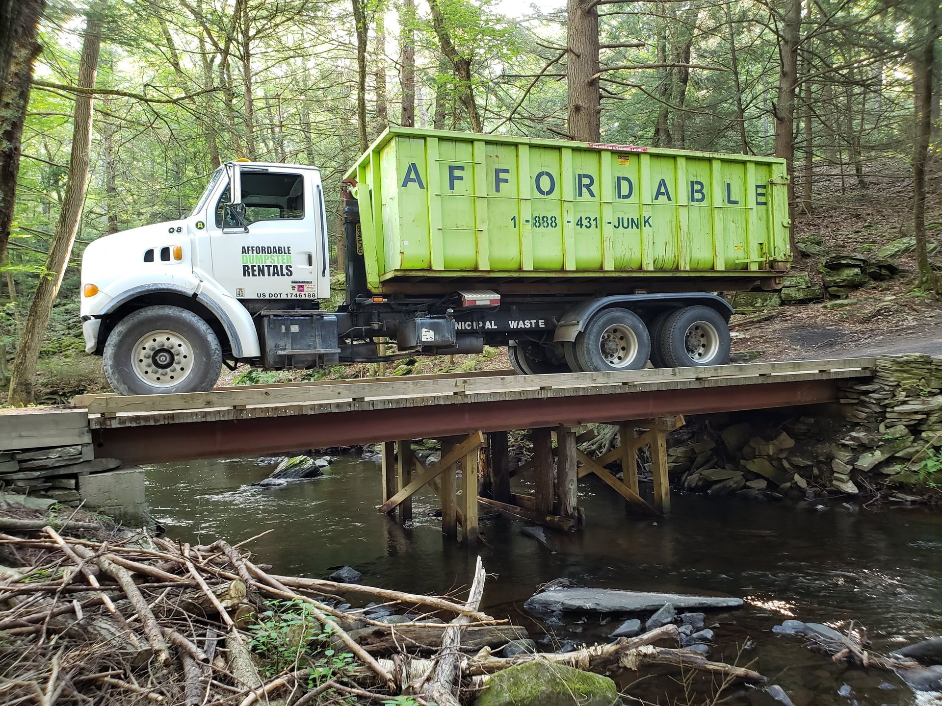 A dump truck is driving over a bridge in the woods.