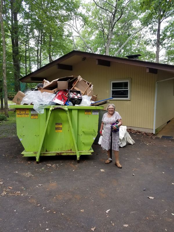 A woman is standing in front of a large green dumpster.