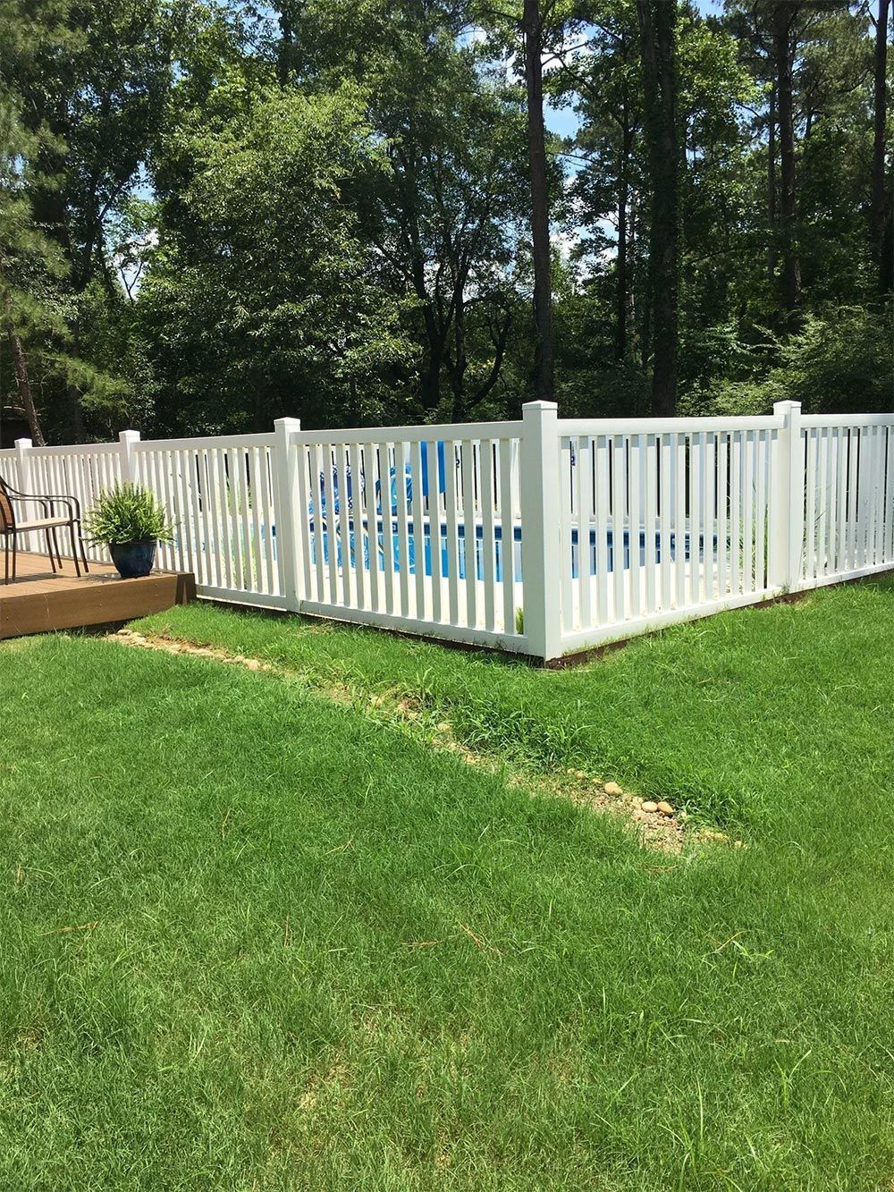 White fenced backyard pool on a green lawn with trees in the background