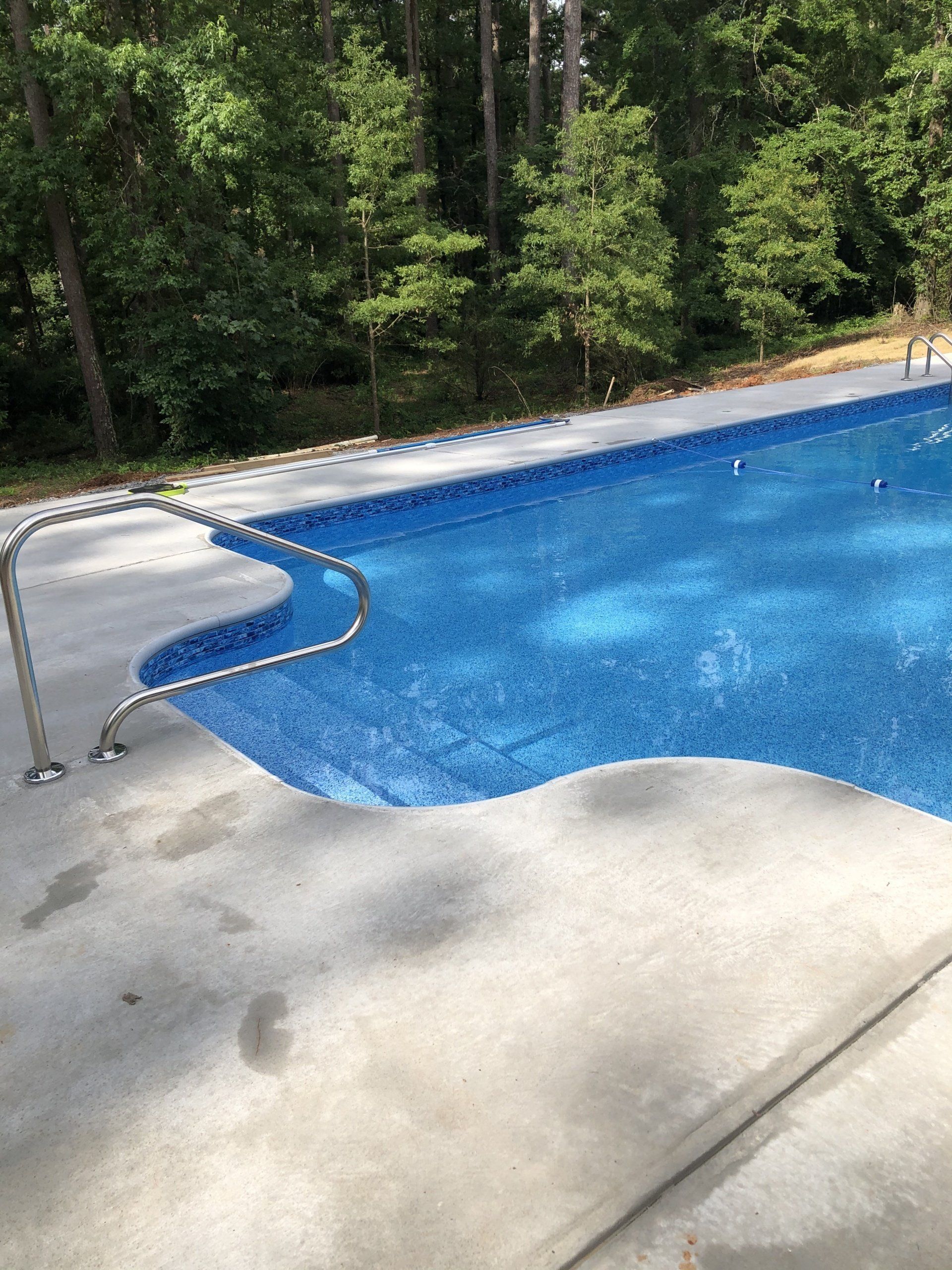 Backyard swimming pool with blue water, curved metal handrail, and trees in the background