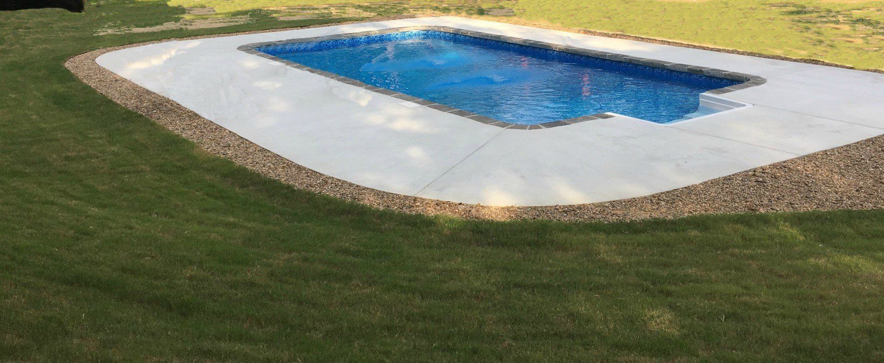 Backyard swimming pool with blue water, white concrete border, and green grass around it