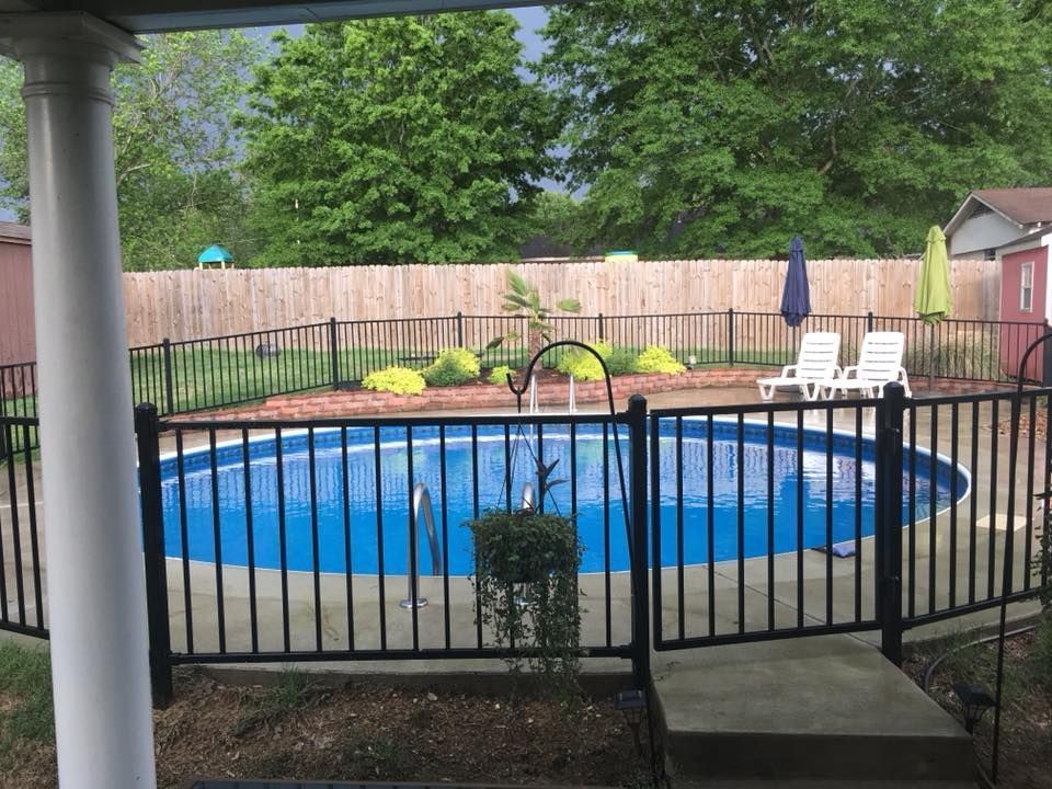 Backyard with a blue above-ground pool, black fence, white chairs, and wooden privacy fence.