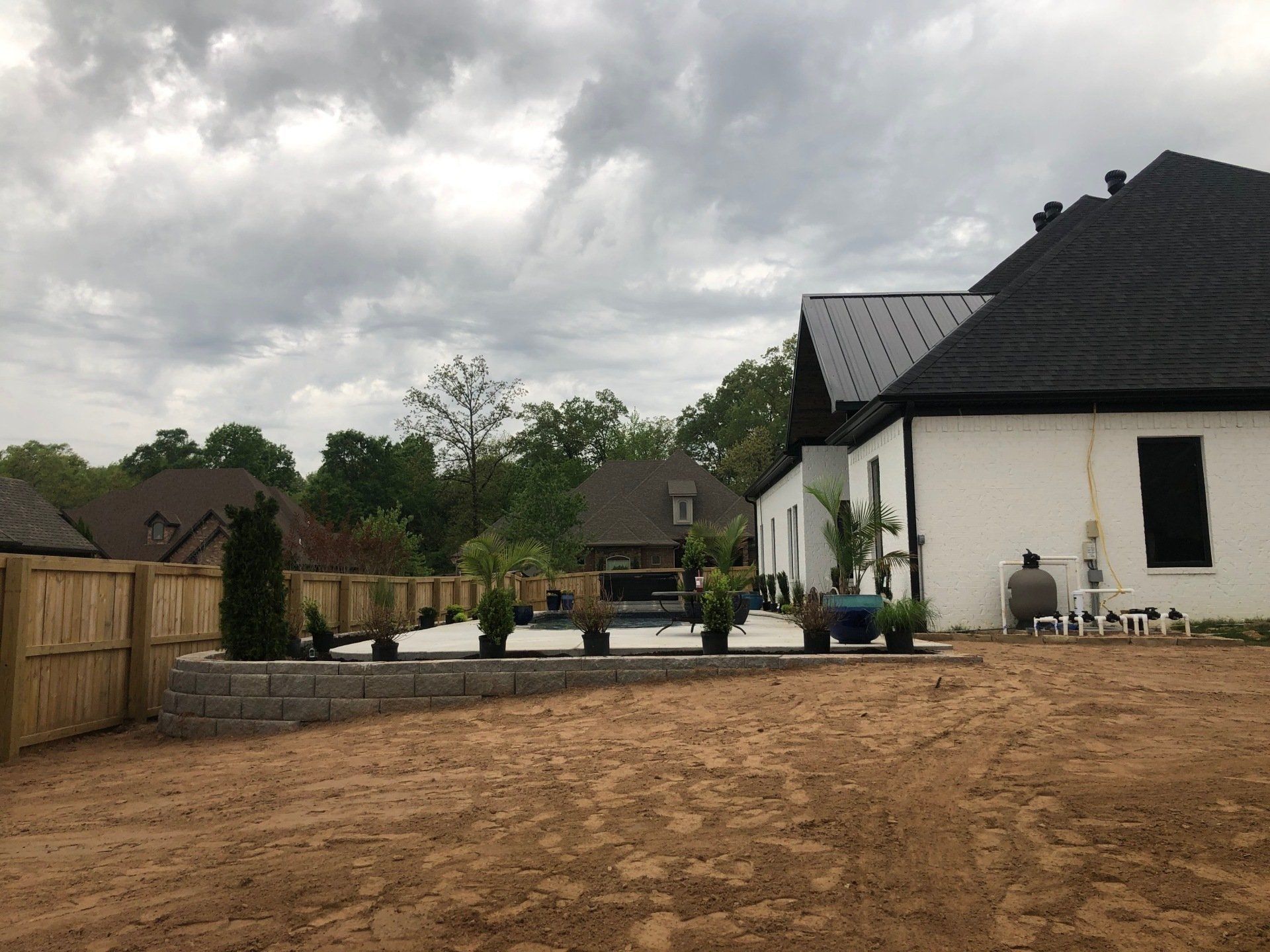 Wide dirt yard beside a white house with a black roof under cloudy skies