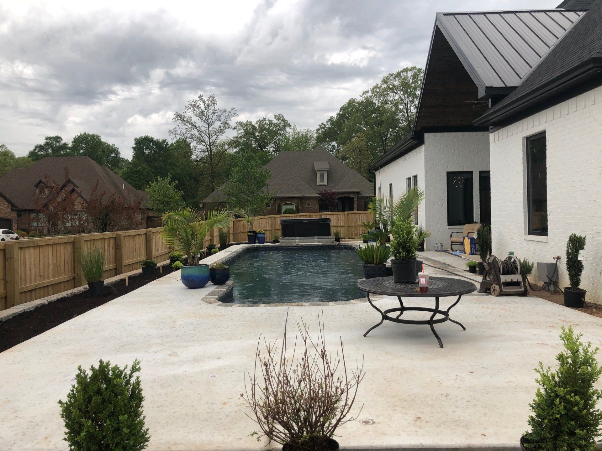 Backyard patio with a swimming pool, white house, and patio furniture under cloudy skies