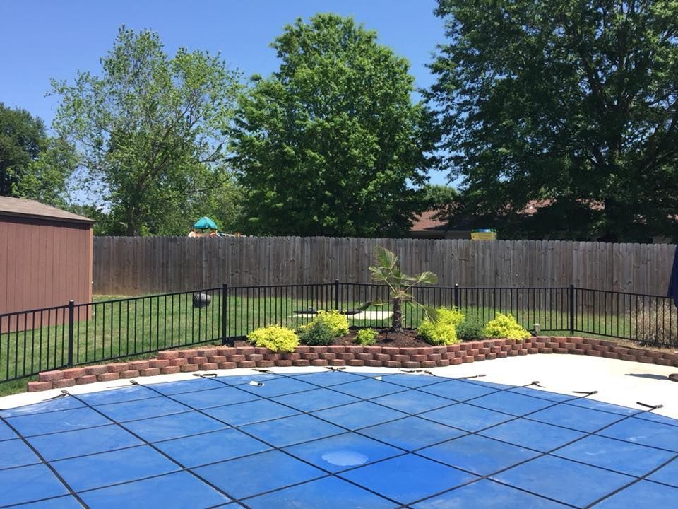 Backyard pool covered with a blue tarp, bordered by a fence, lawn, and trees under a clear sky
