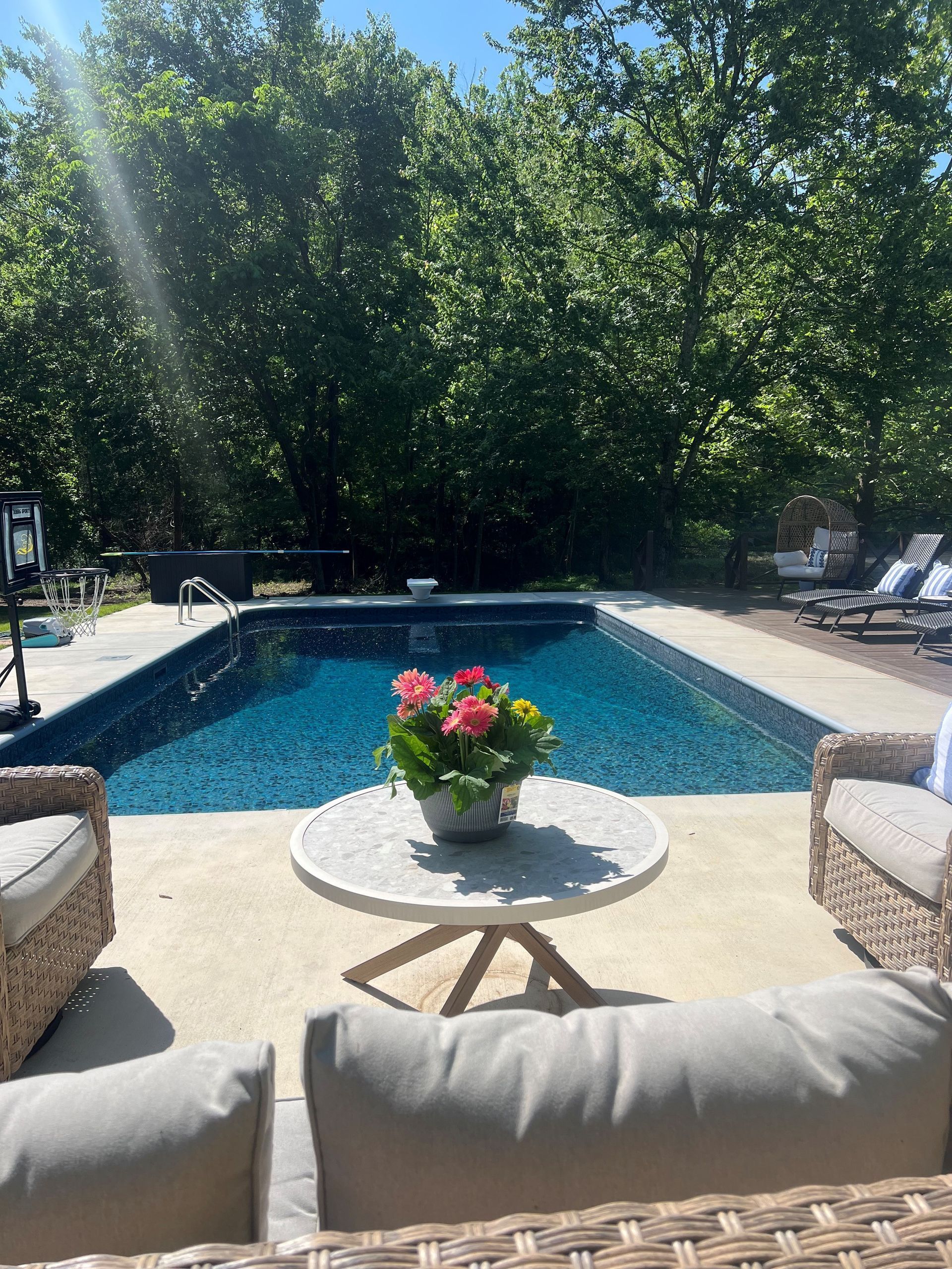 Backyard pool with wicker chairs, cushioned seating, and a flower vase on a small table in the foreground