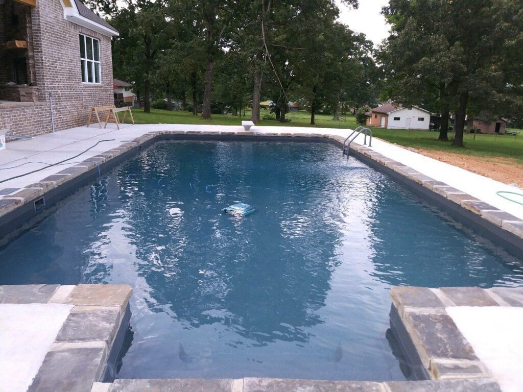 Rectangular backyard swimming pool with blue water beside a stone house and patio.