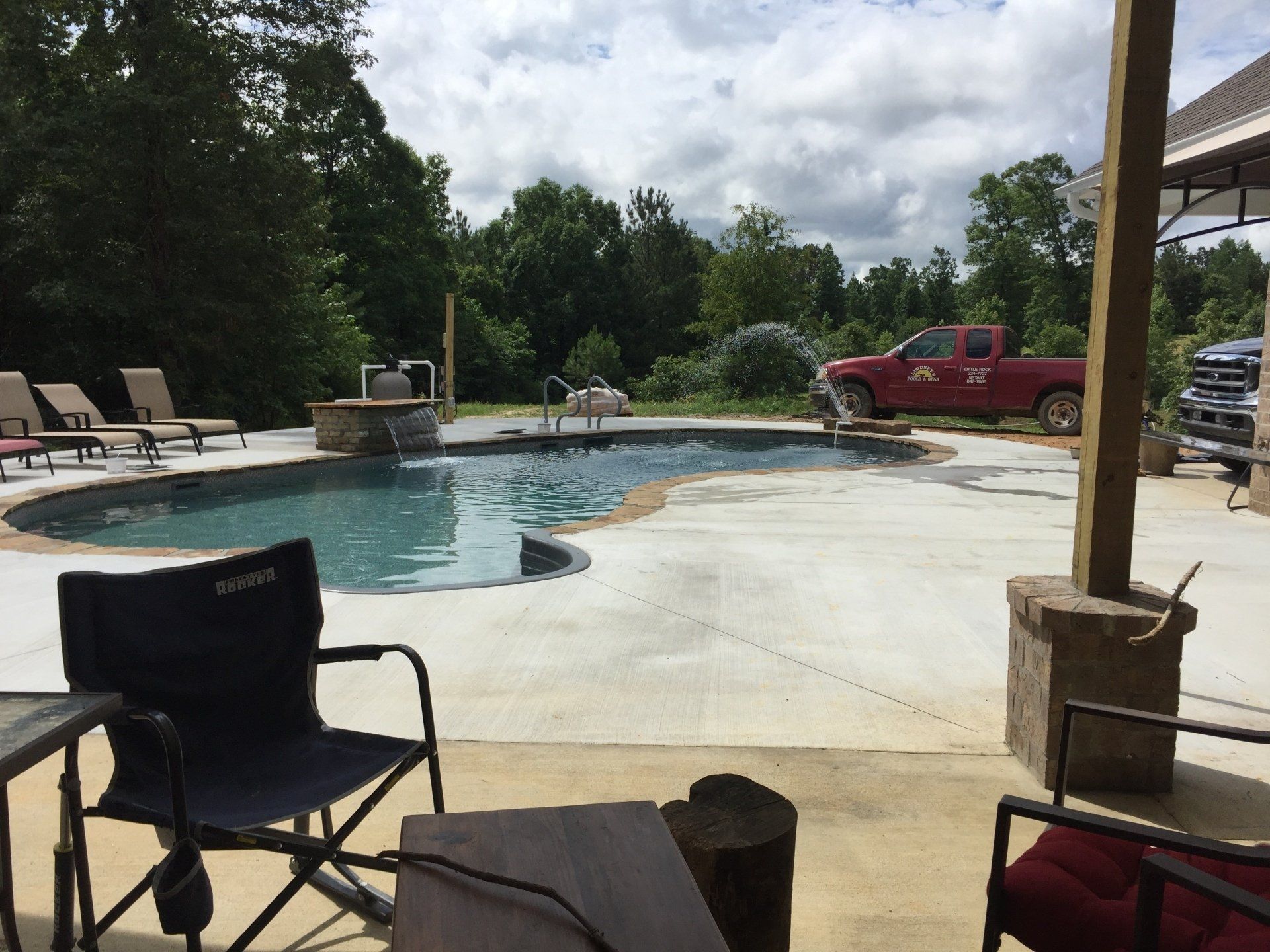 Backyard pool with lounge chairs, a red truck, and a black folding chair in the foreground
