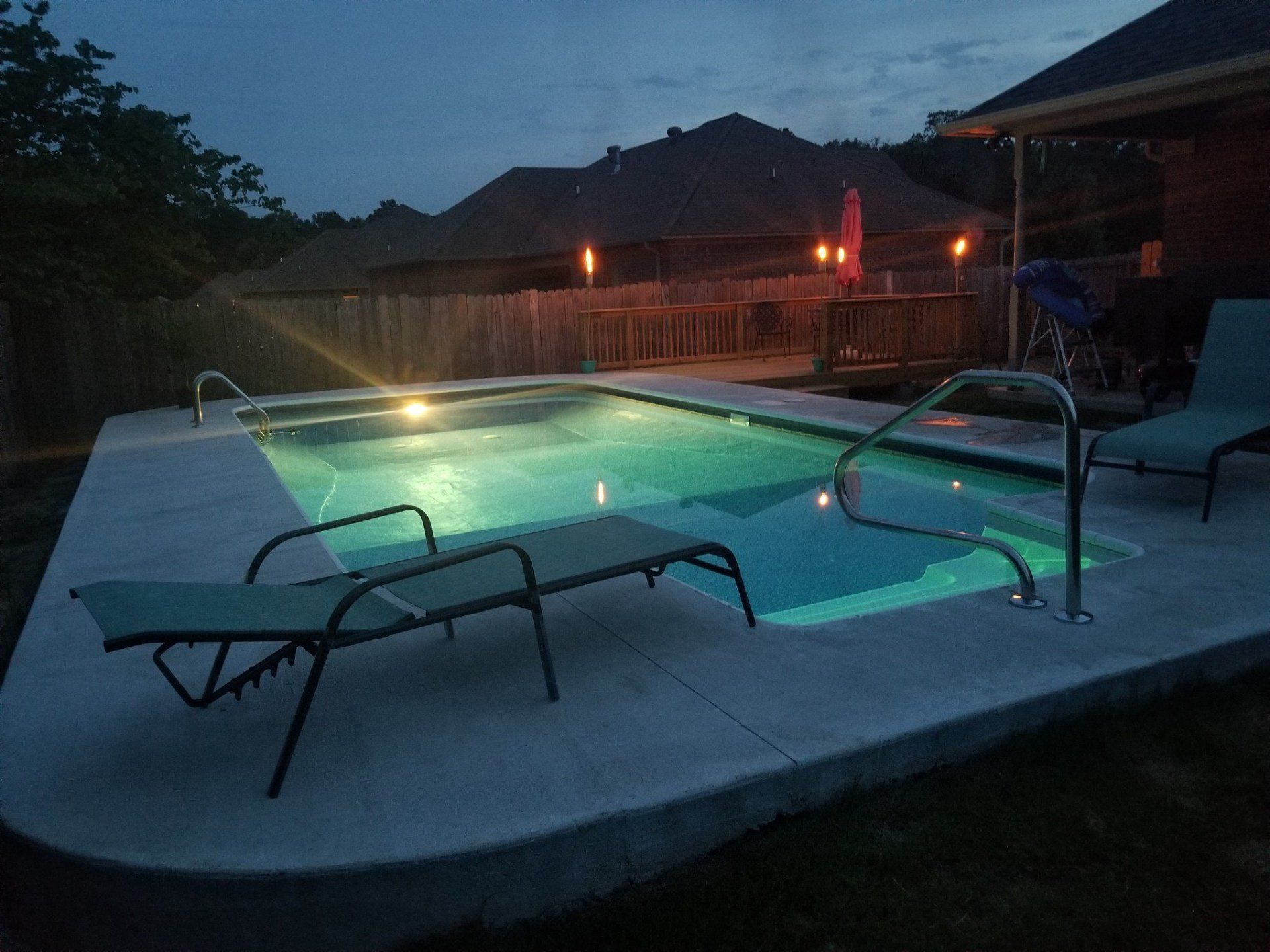 Backyard hot tub lit at dusk beside a fenced yard and mountains in the background