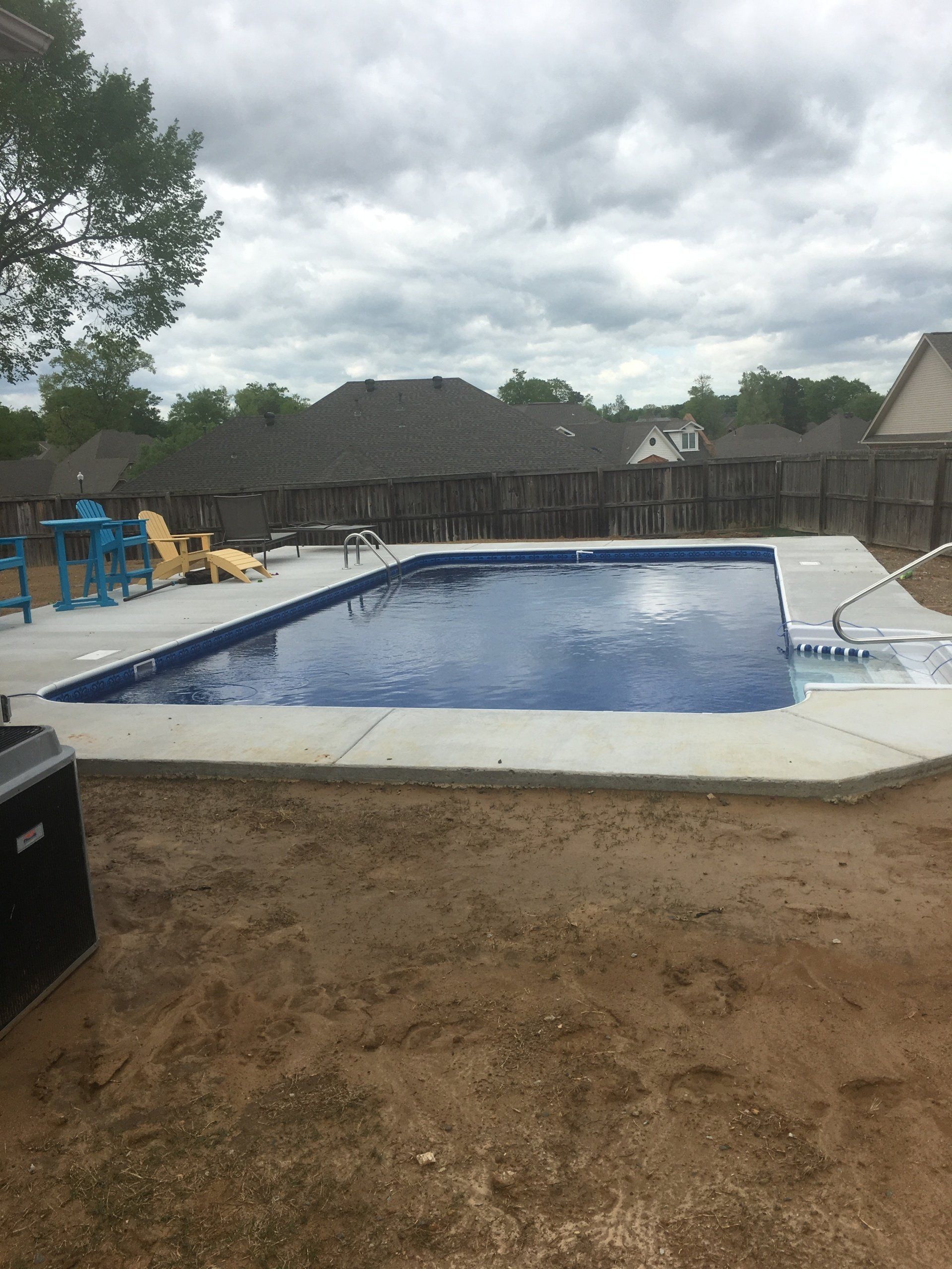 Backyard swimming pool with blue water, patio furniture, and a cloudy sky