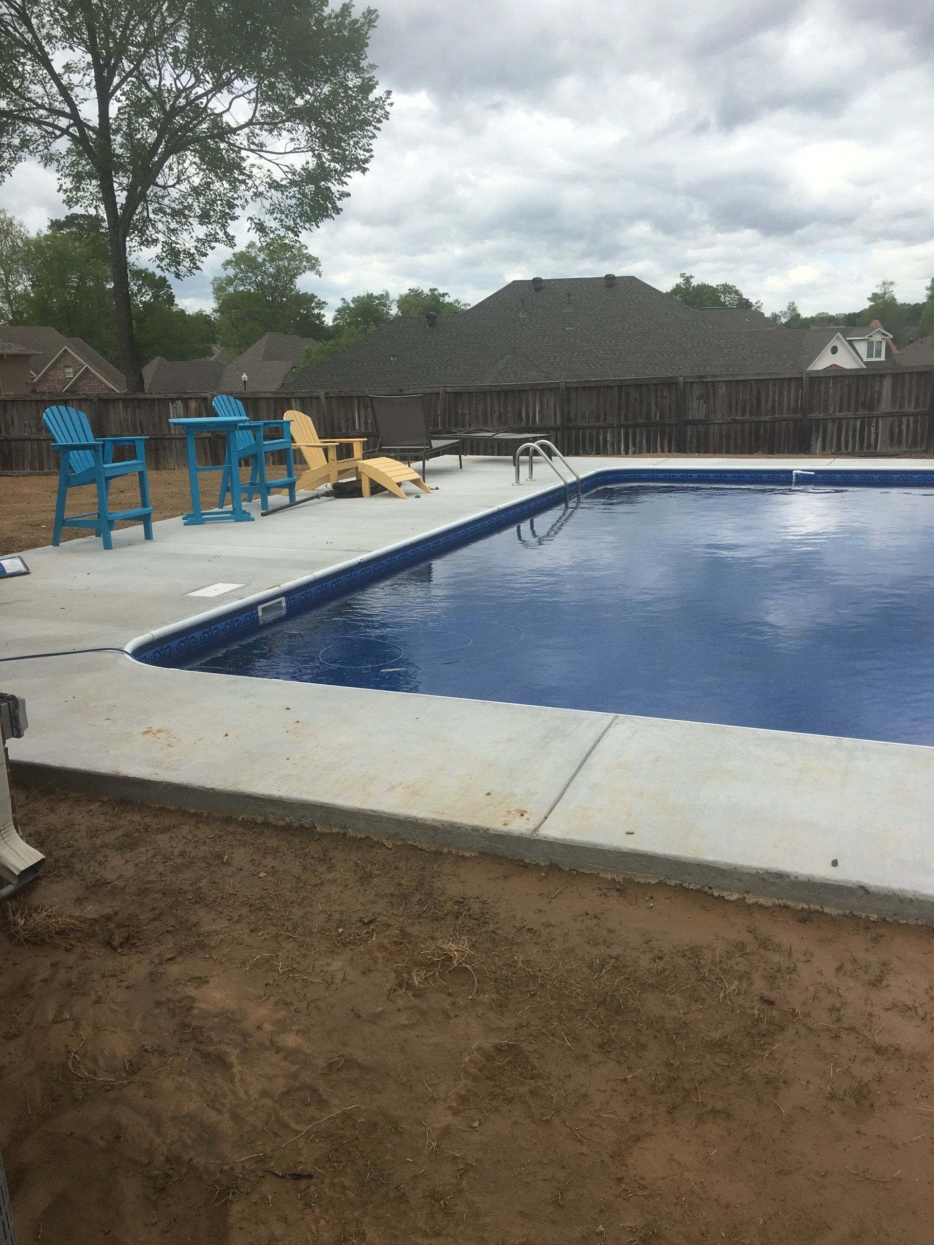 Outdoor swimming pool with blue water, lounge chairs, a tree, and thatched-roof buildings in the background