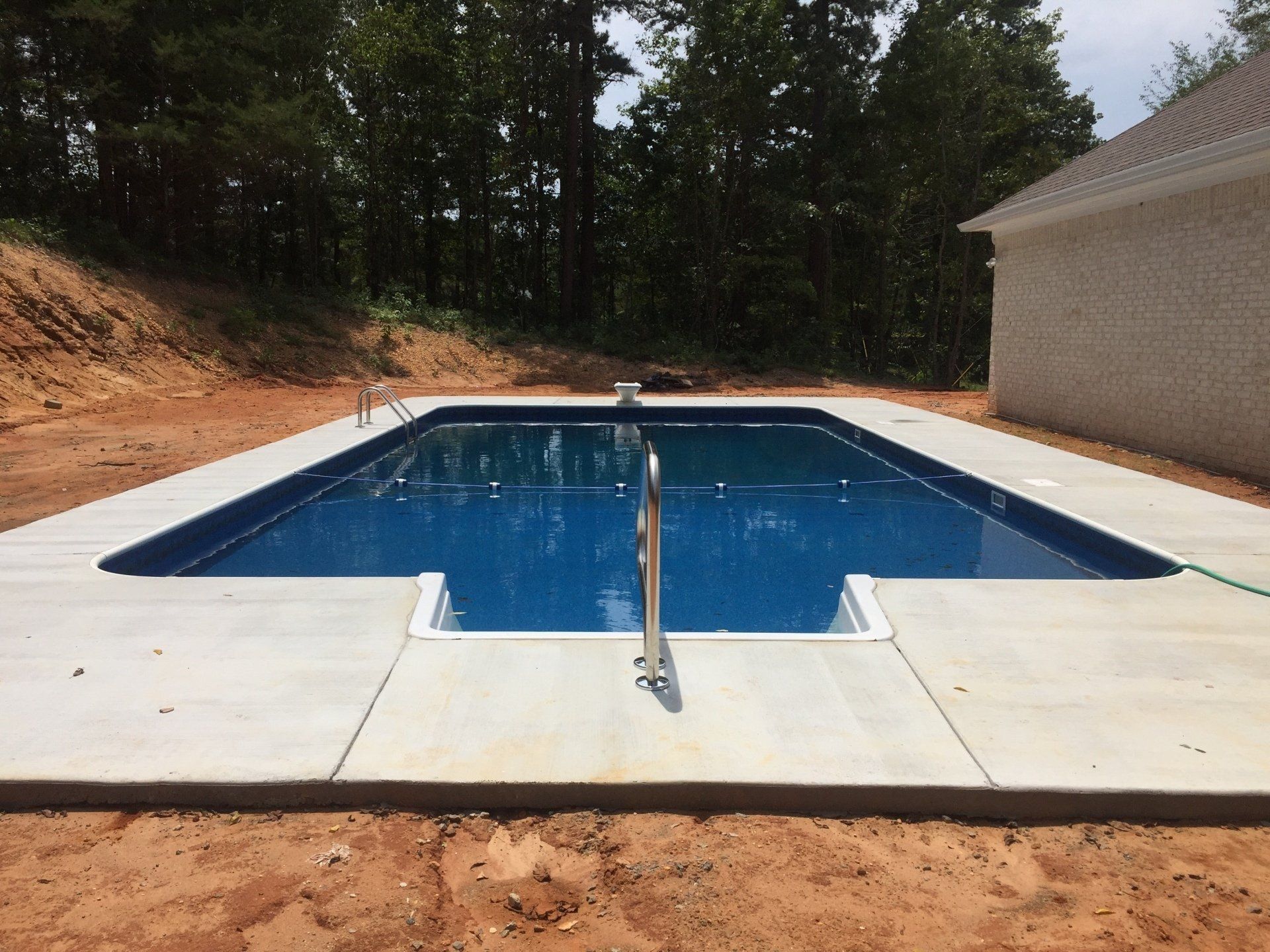 Outdoor backyard swimming pool with blue water, diving board, and concrete deck beside a building and trees