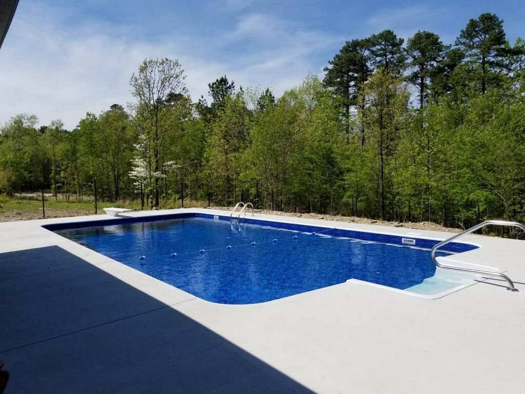 Outdoor swimming pool with blue water, white deck, and trees in the background