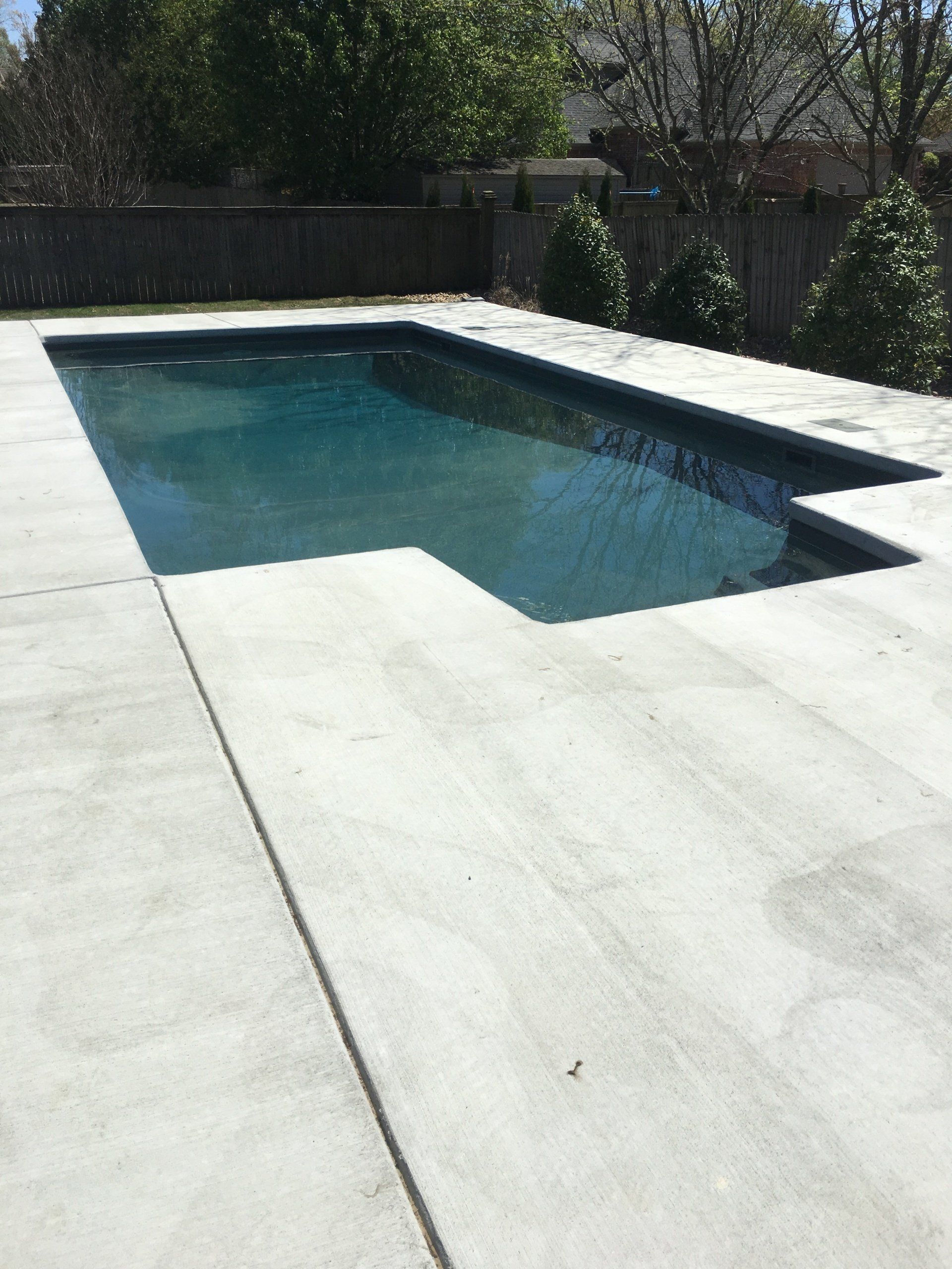 Empty backyard swimming pool with clear blue water and white concrete deck in sunlight