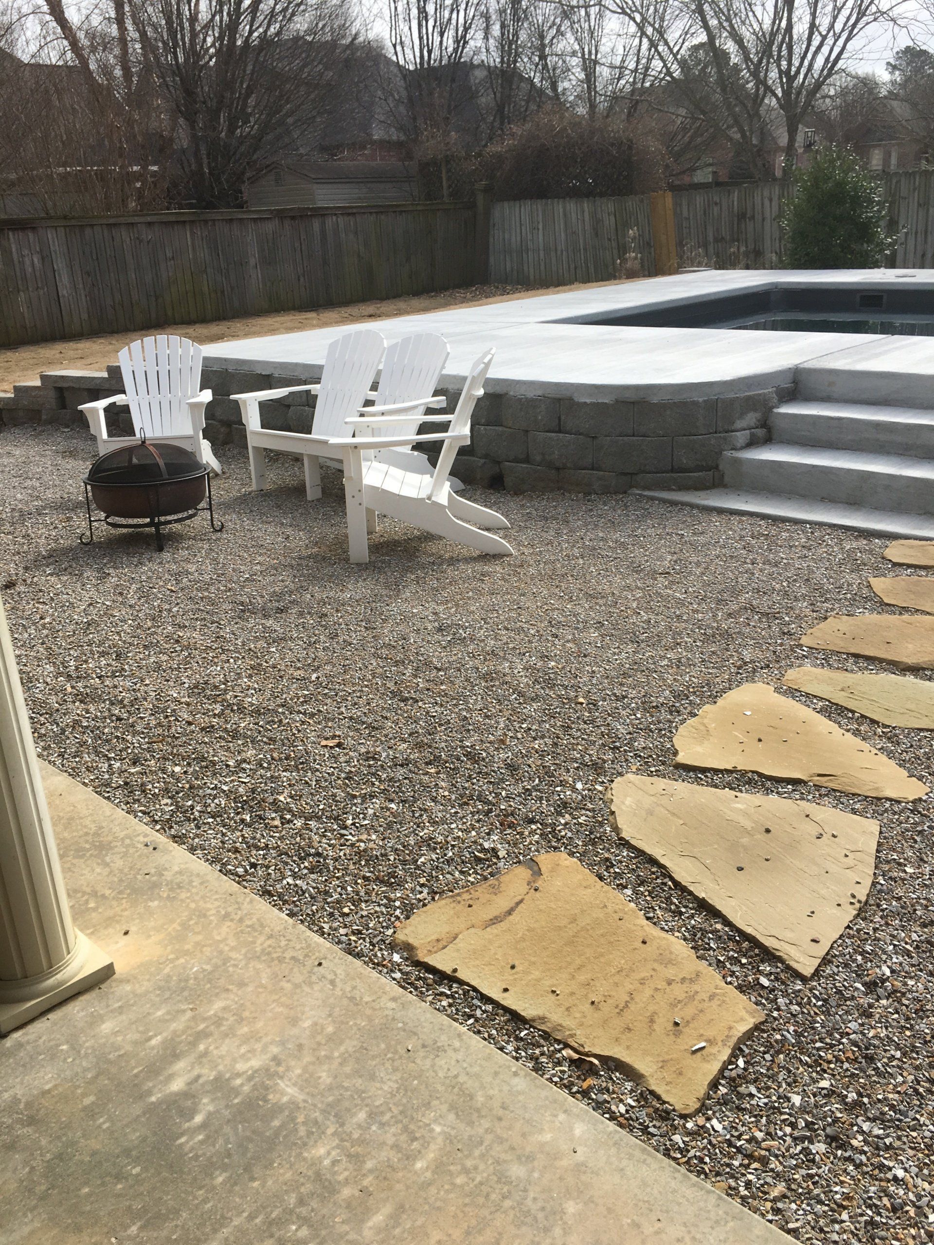 Backyard patio with white Adirondack chairs, a fire pit, gravel ground, and stone steps by a raised deck