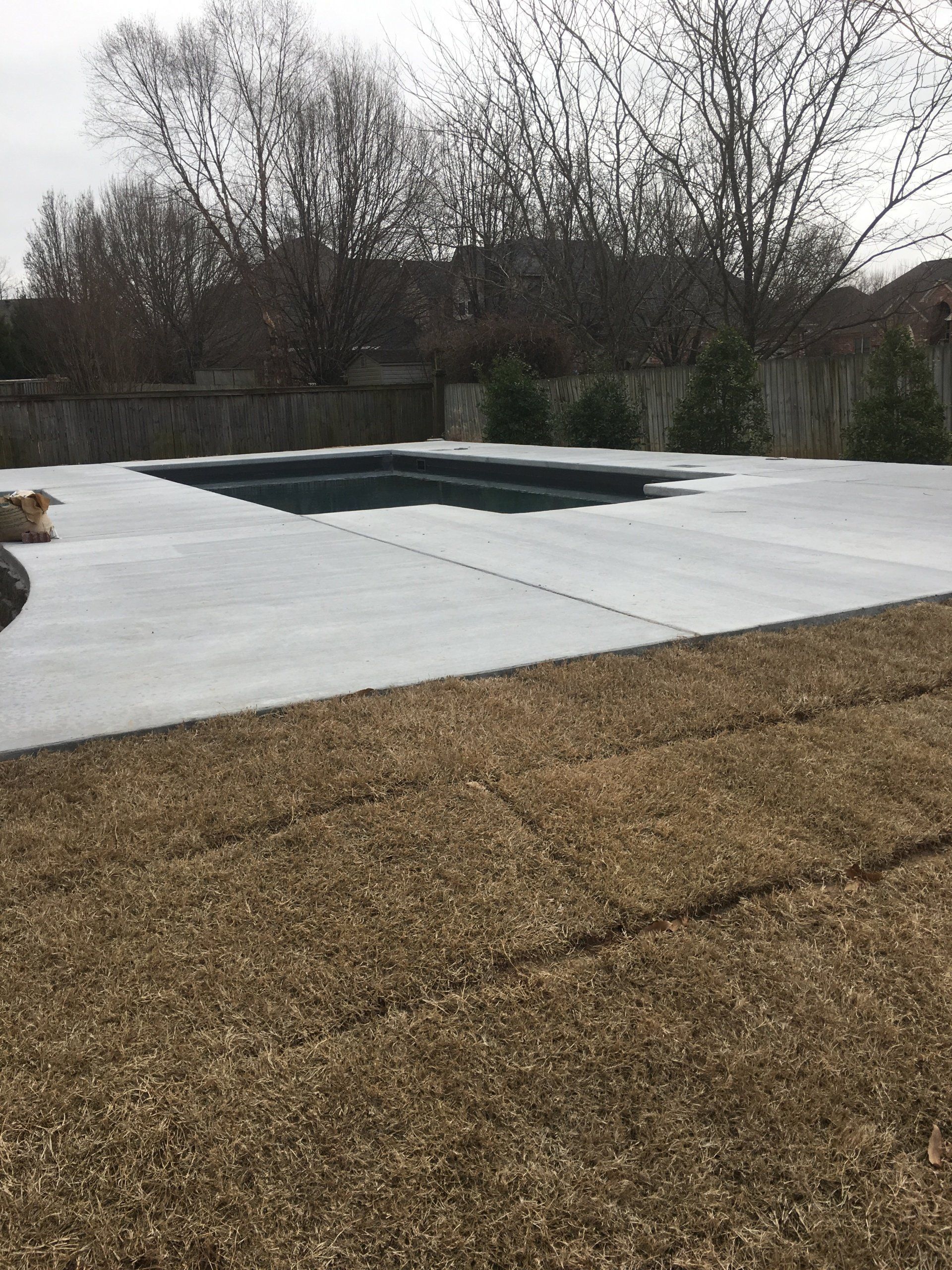 Rooftop with a white membrane area and dark rectangular patch, surrounded by trees under an overcast sky