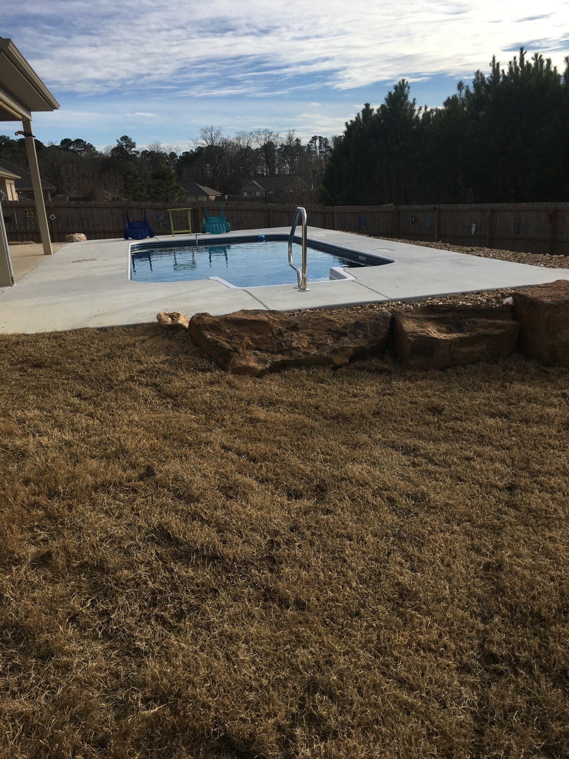 Backyard pool with a white patio, small blue pool, and dry brown grass in the foreground