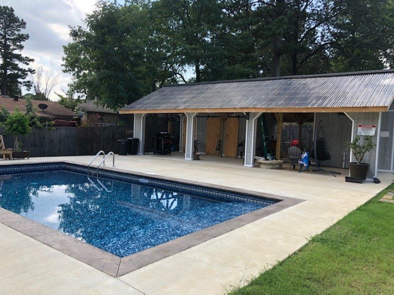 Backyard swimming pool beside a covered patio with white columns and trees beyond