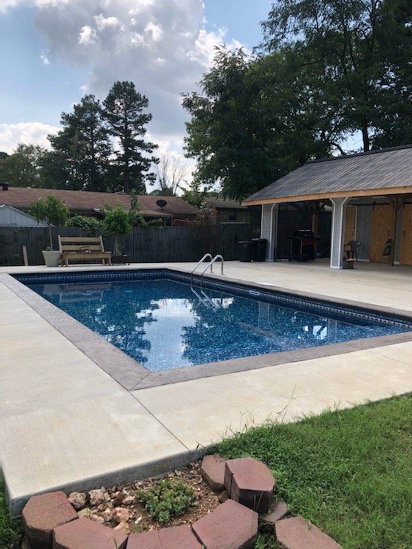 Backyard swimming pool with patio, trees, and a garage in the background