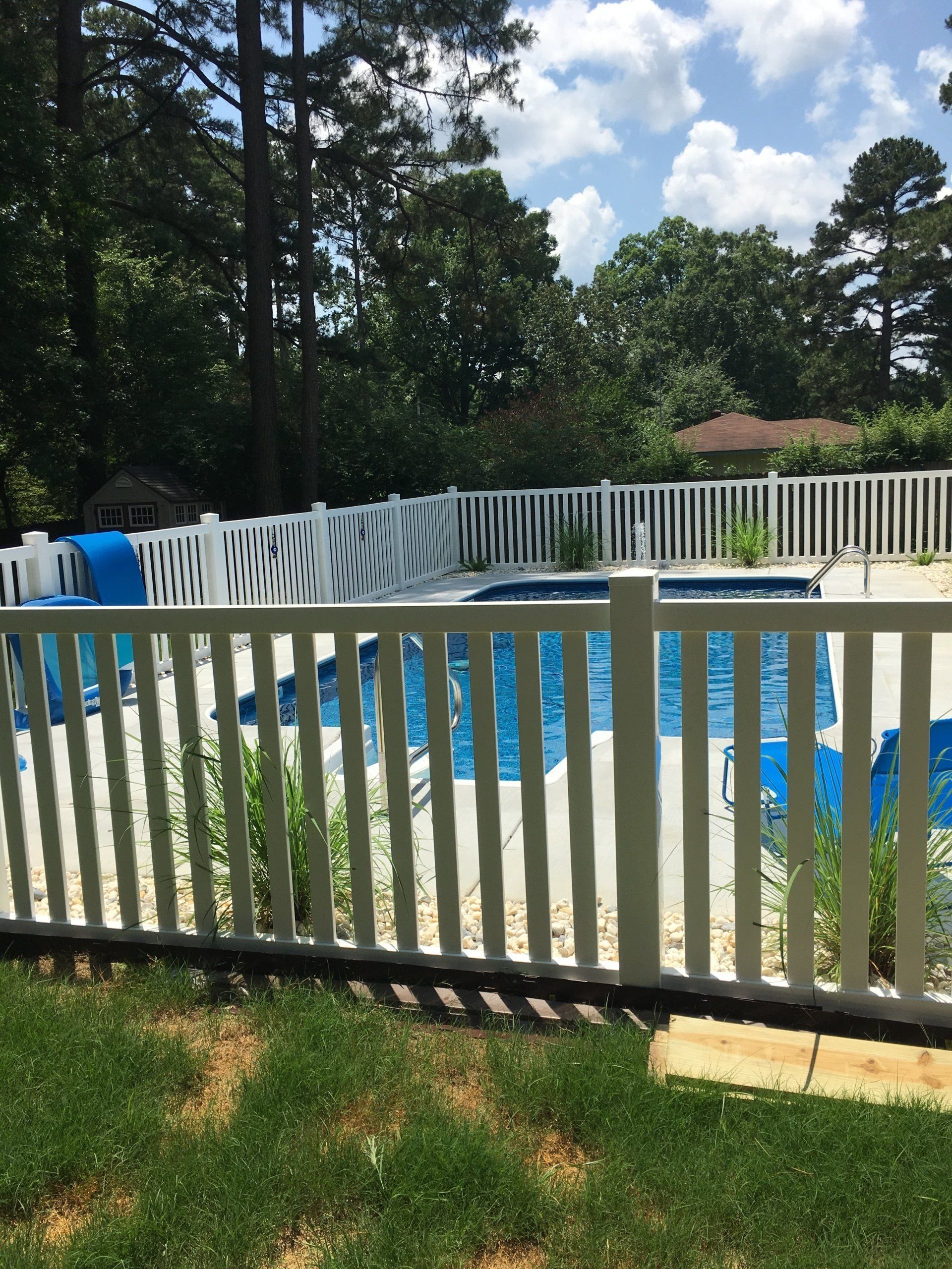 Backyard pool with blue cover, white fence, and trees under a sunny sky