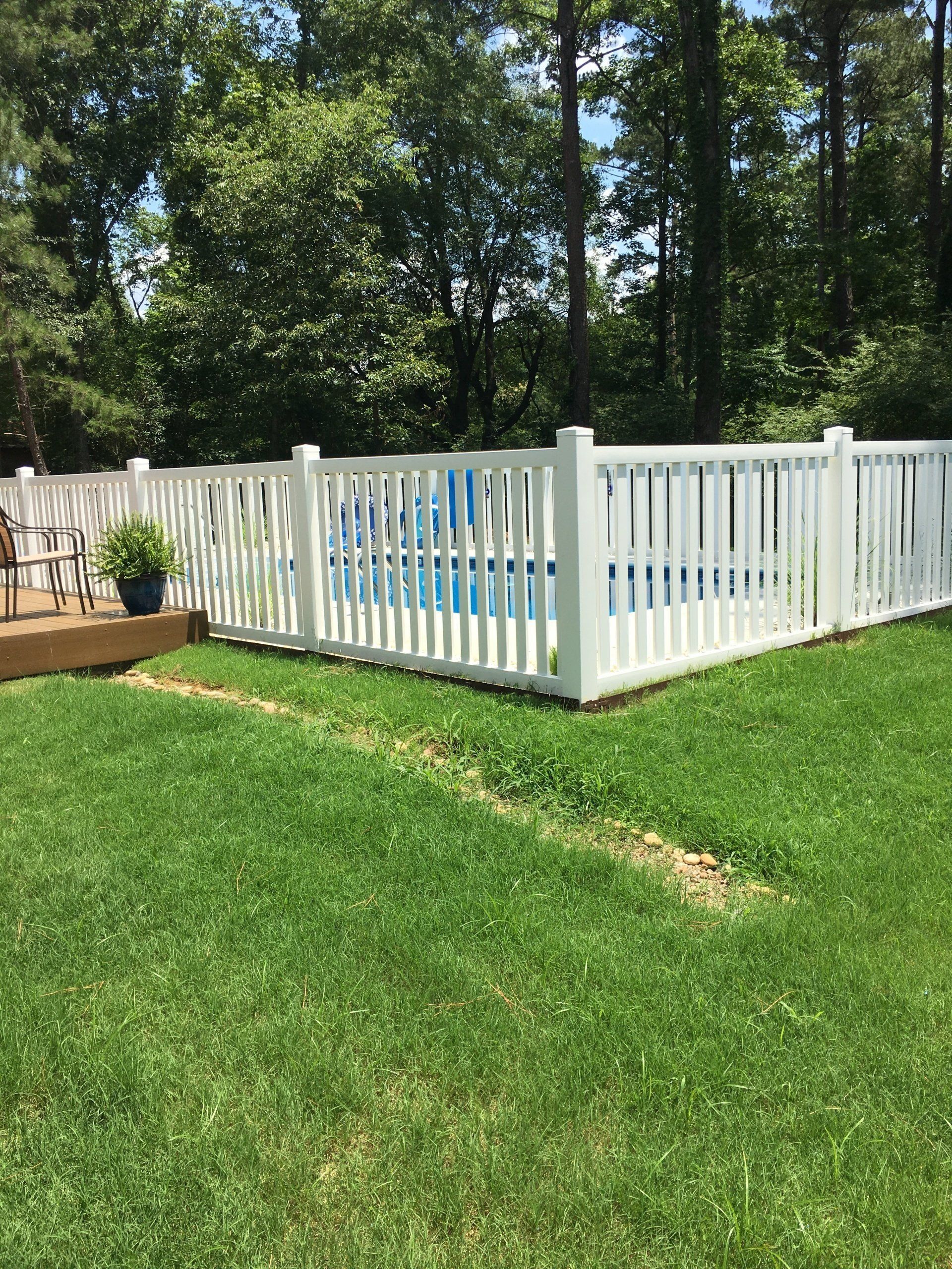 White fenced backyard with a blue above-ground pool on a green lawn, trees in the background