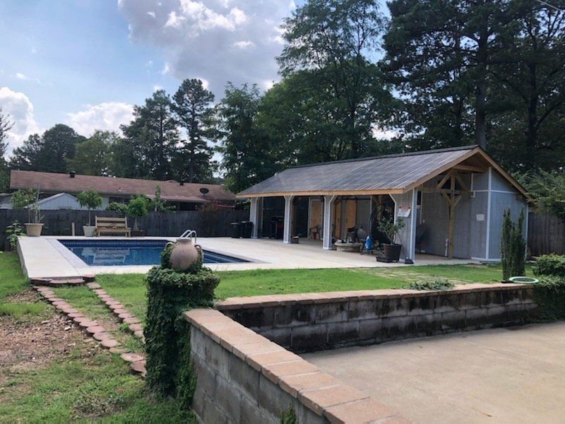 Backyard with a swimming pool, patio pavilion, and stone retaining wall surrounded by trees