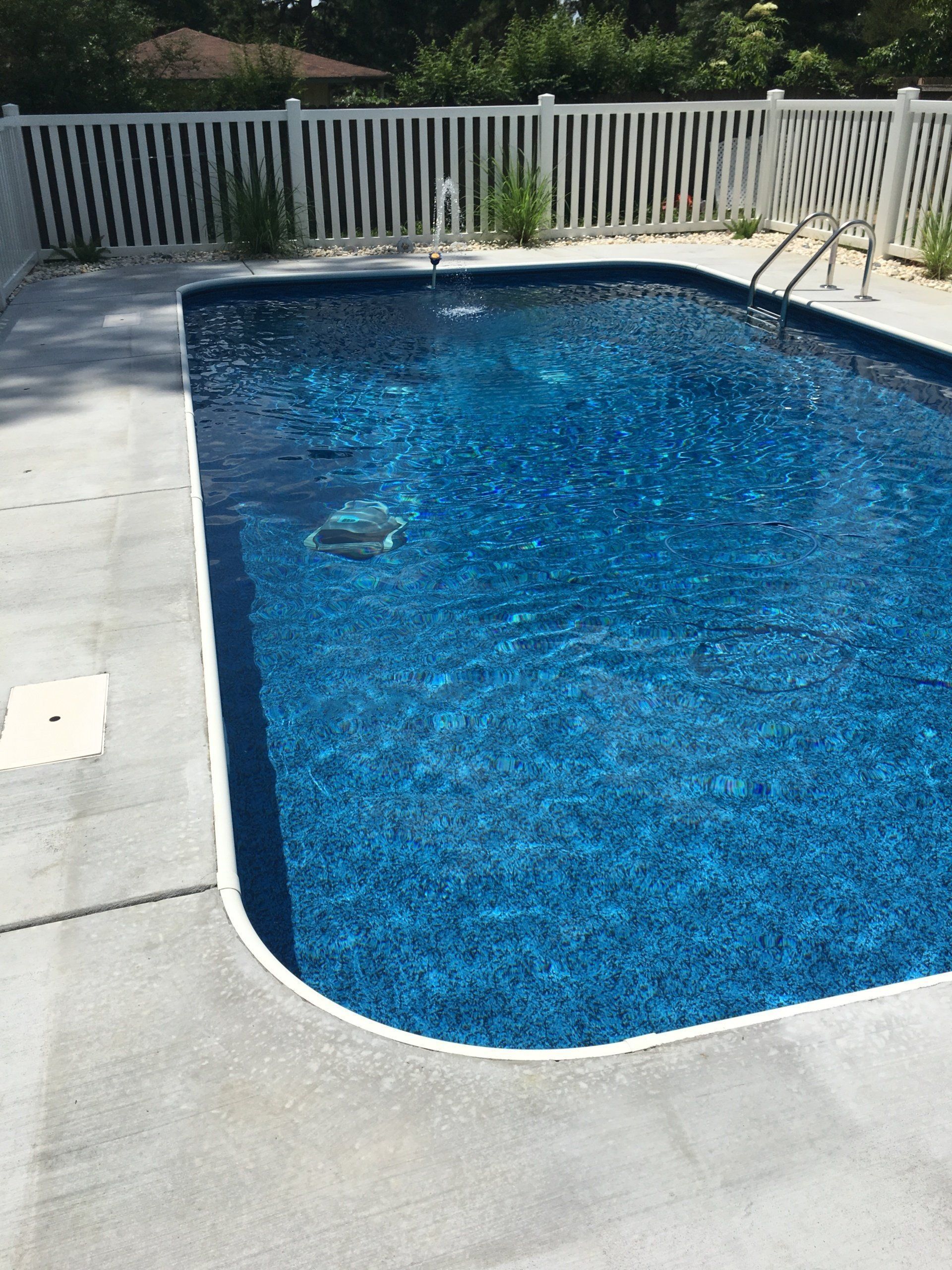 Backyard swimming pool with blue water, light deck, and white fence in the background